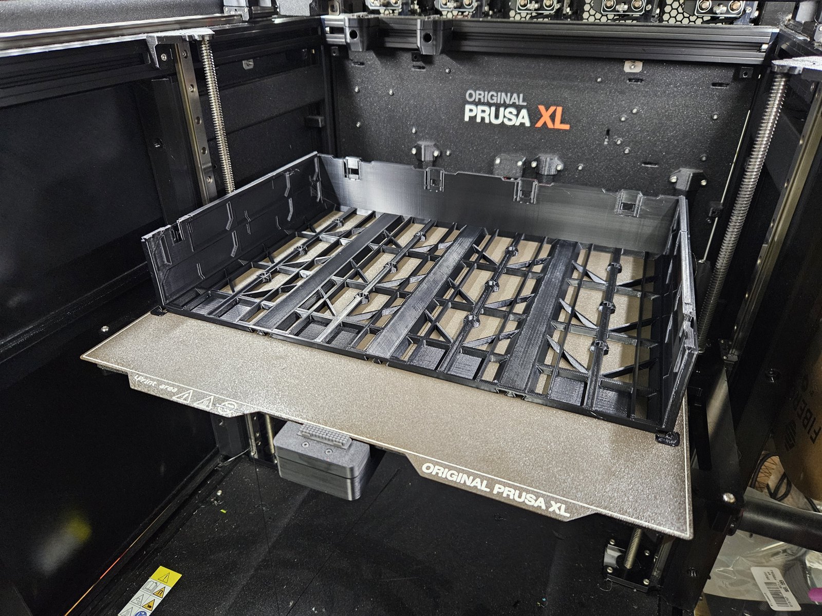 A wide black MODULITH case, just printed, sitting on the textured build plate of an Original Prusa XL