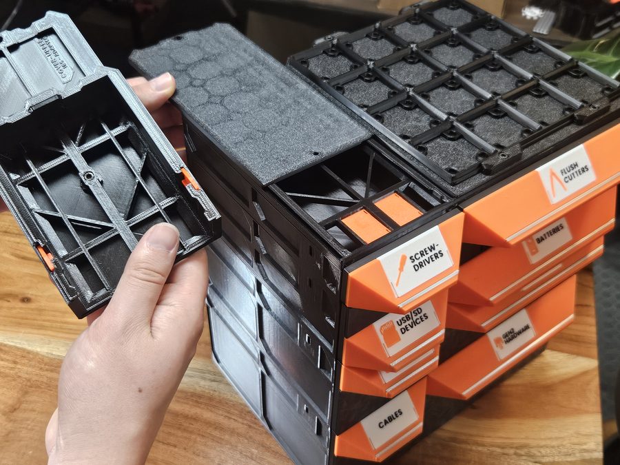 A hand bringing a shallower case up to the Size Adapter Cover on top of a deeper tabletop build of orange drawers