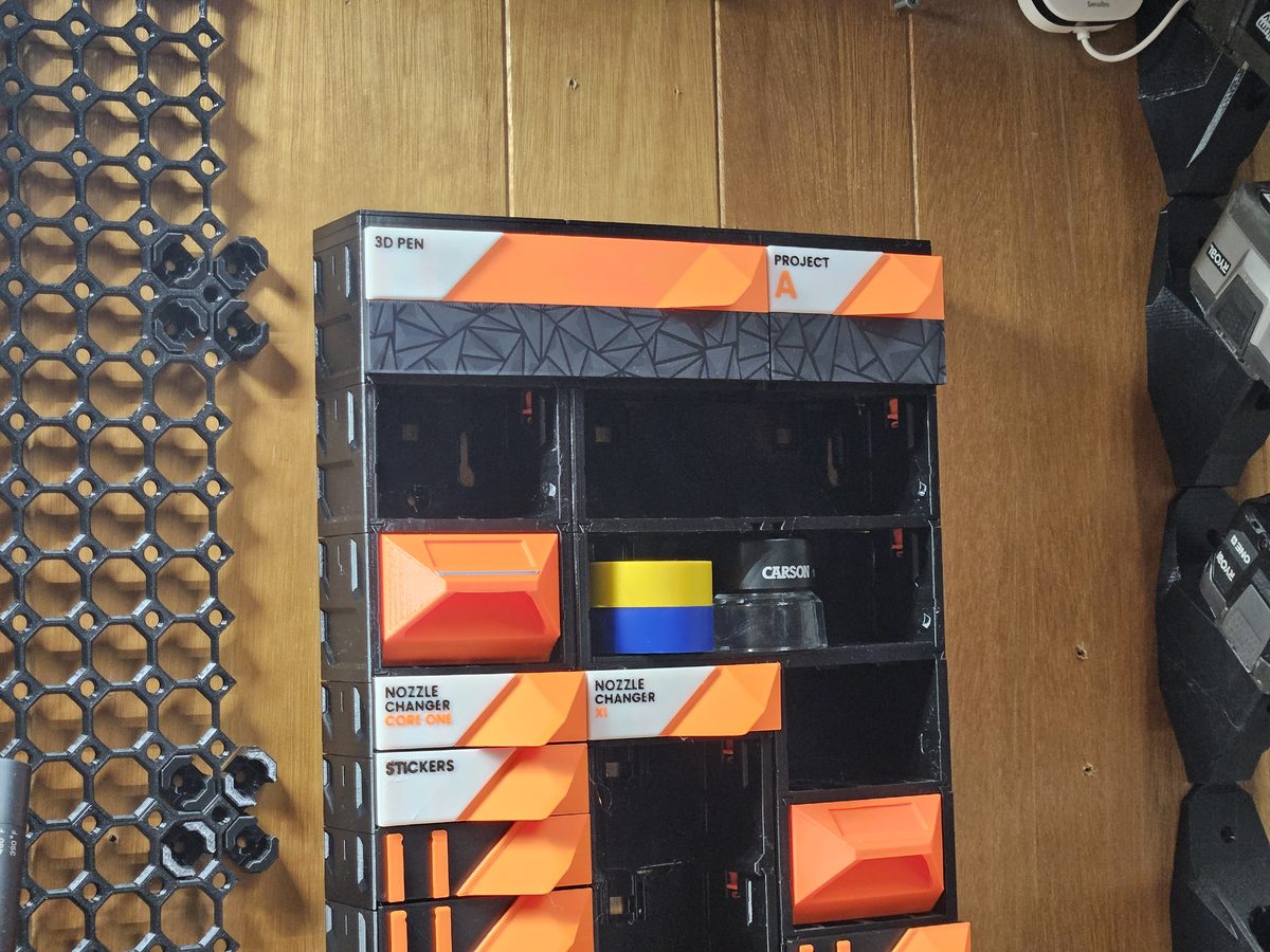 A finished wall build: a column of cases with orange drawers and open shelf bays hanging beneath the top row on a wood-panelled wall