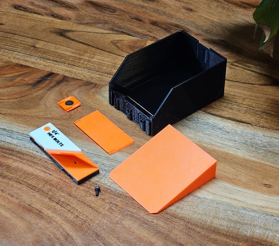 The parts laid out: bin body, screw-hole cover, Gravity Wedge, magnet insert, labeled faceplate, and the M3 screw
