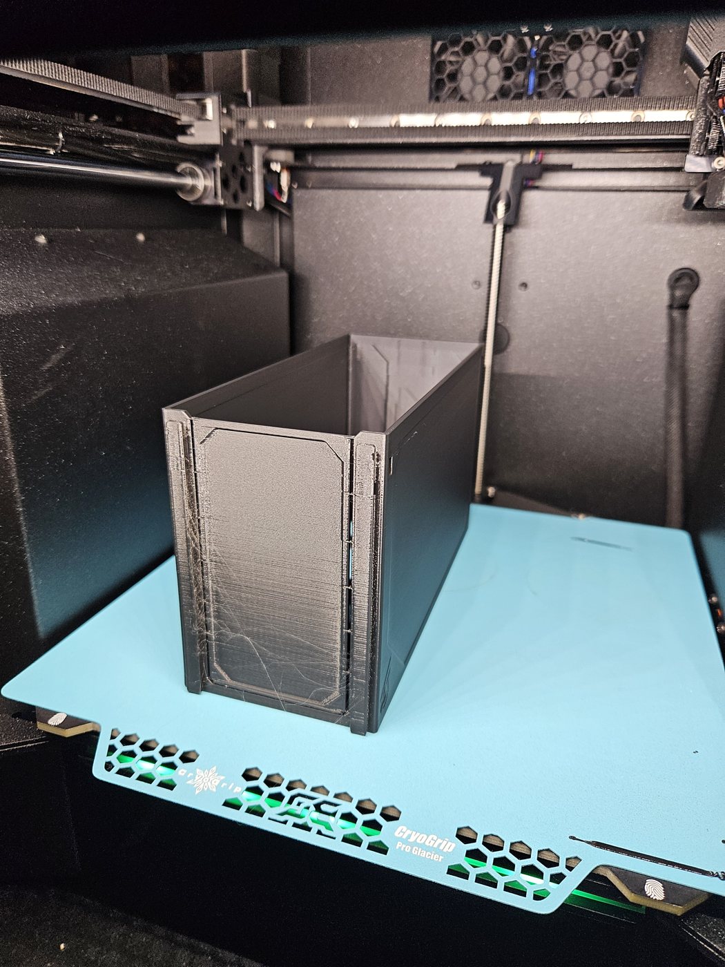 A tall black drawer standing upright on a turquoise build plate inside an enclosed printer, just finished
