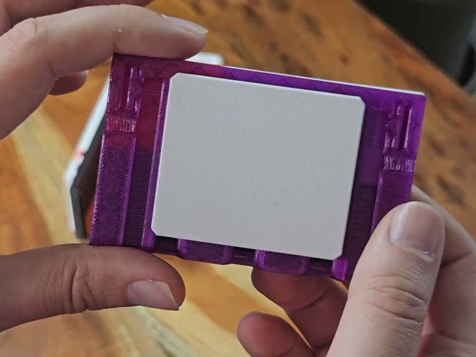 The back of a translucent purple faceplate held in two hands, a flat gray back cover seated in it