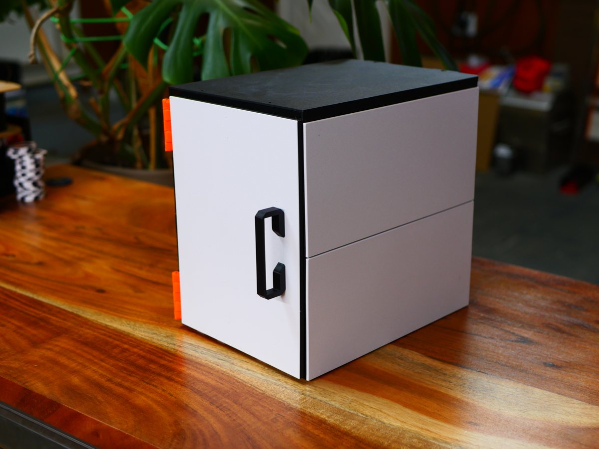 A two-high cabinet on a wooden counter, its white door closed, black handle, orange hinges