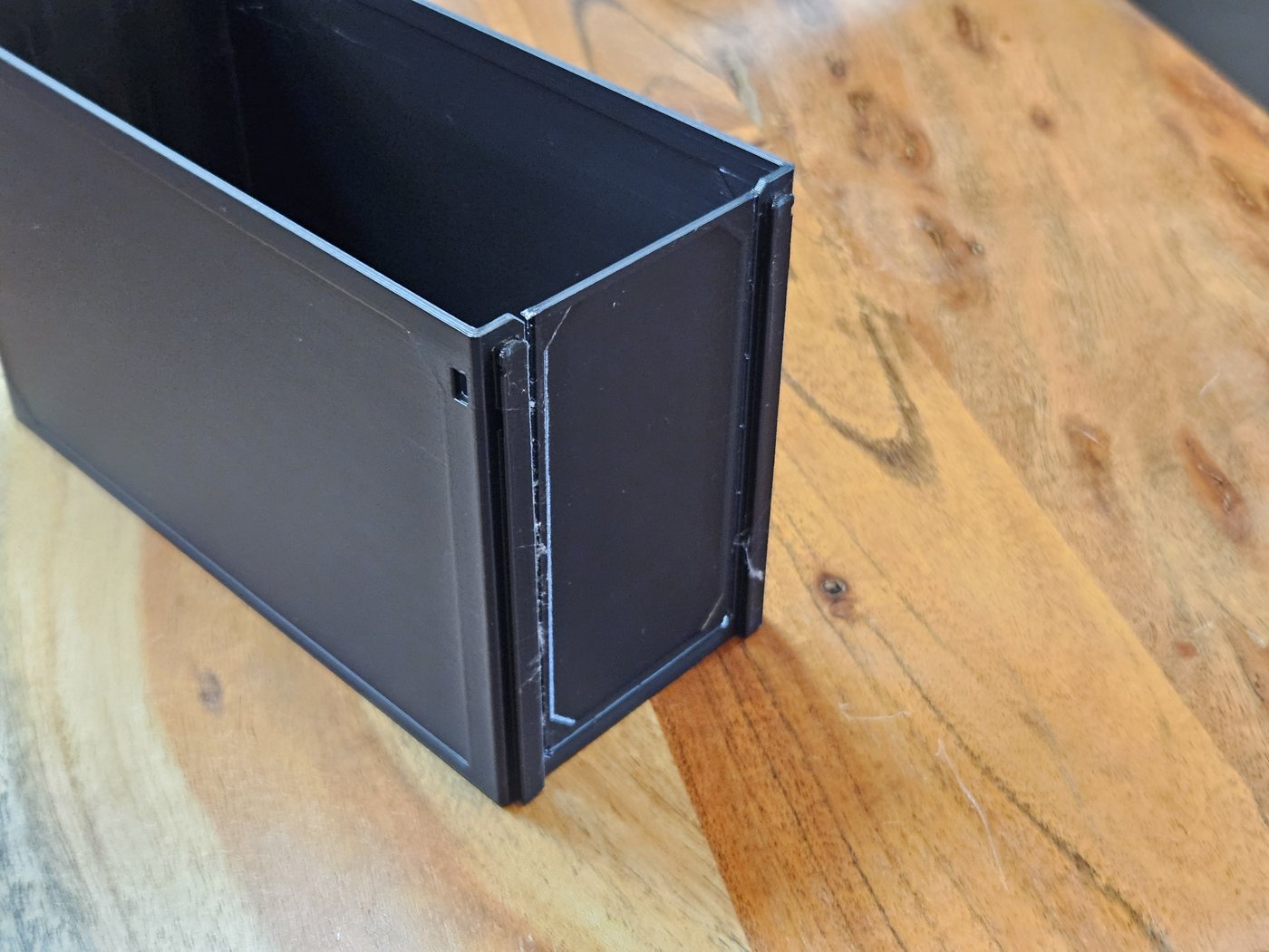 A printed Gridfinity Decor drawer standing on a wooden bench, a 185 1W-2H, its thin tear-away front still in place across the open end