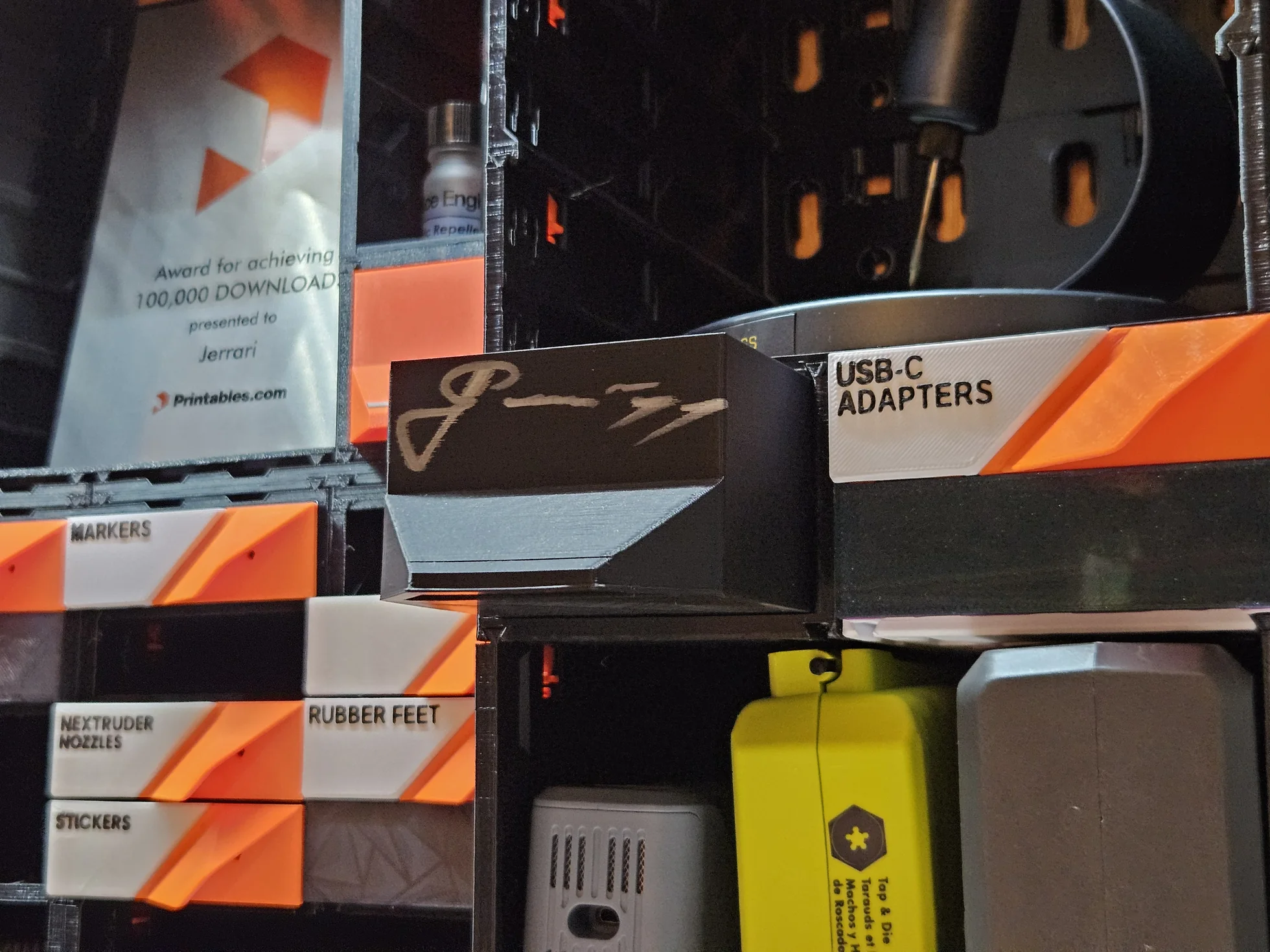 A black drawer printed and signed in 2019, seated in a current case inside a wall build of orange drawers.