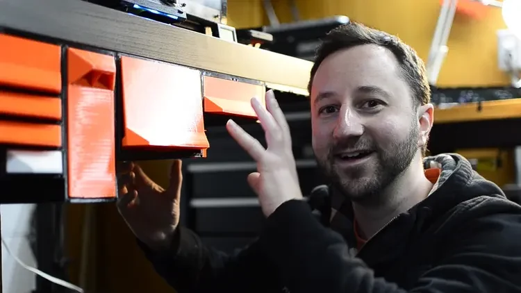 Jerrari at the workbench, mid-explanation, orange drawers under the desk behind him.