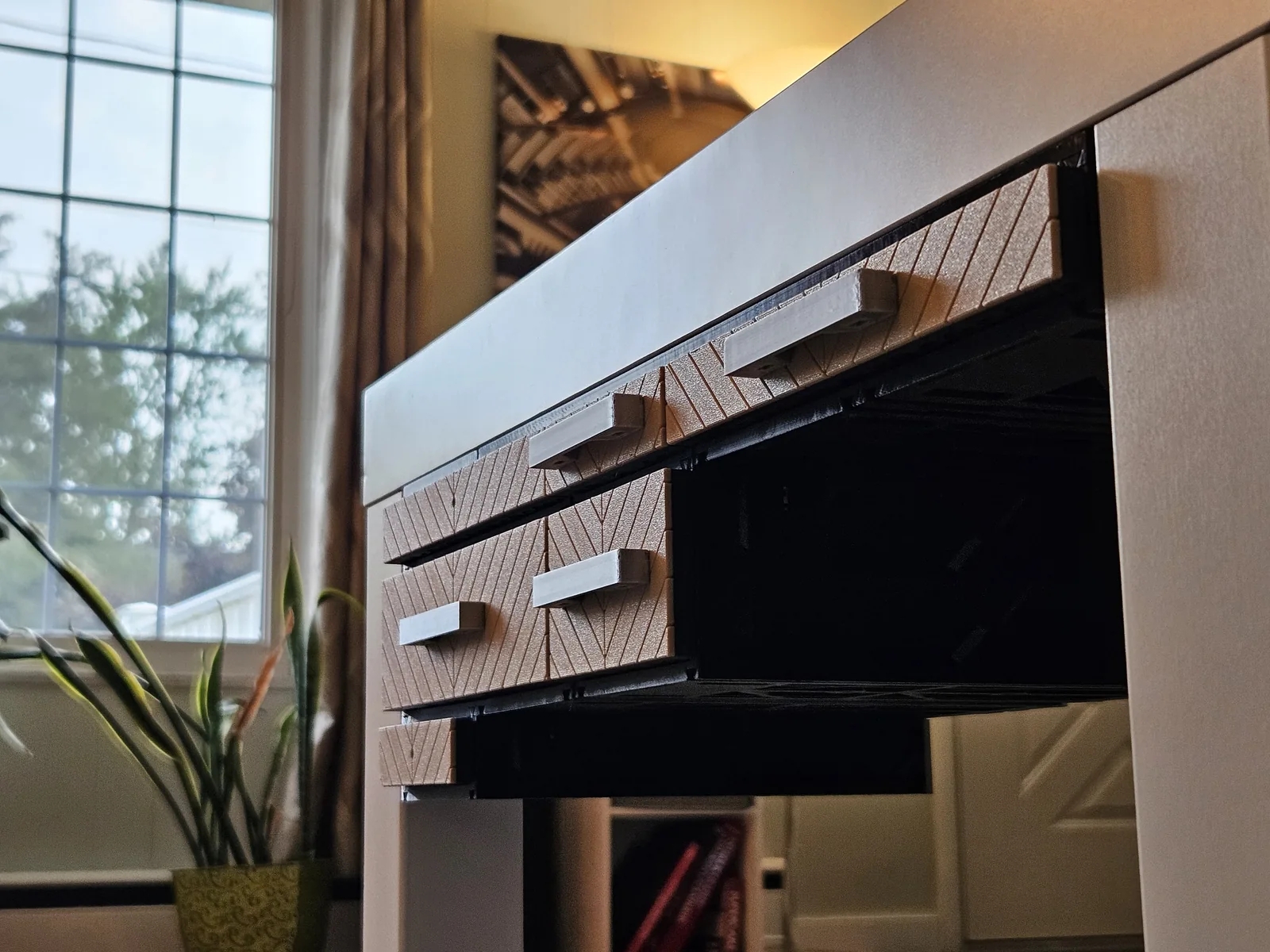 Chevron-fronted MODULITH drawers under a white living-room console, window light and a plant beside them.