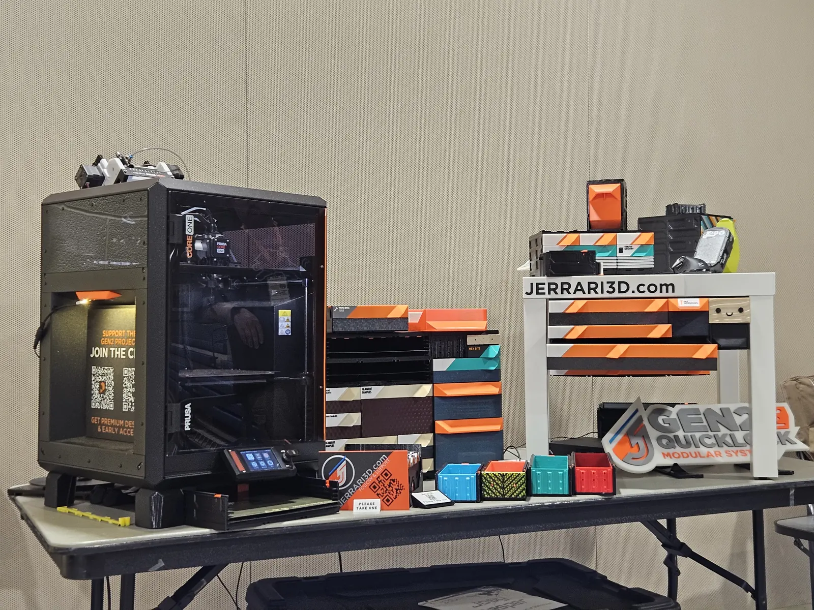 The booth at 3DPrintopia 2025: a Prusa CORE One printing beside kits, sample builds and the jerrari3d.com table.